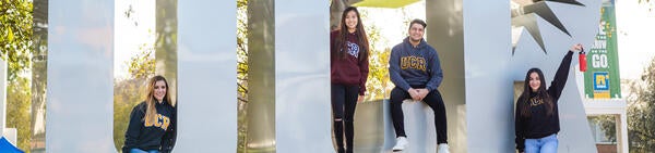 Students wearing UCR gear from Campus Bookstore at UCR Sign